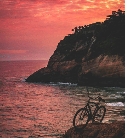 bicicleta acima de uma pedra em frente ao mar com um morro atrás